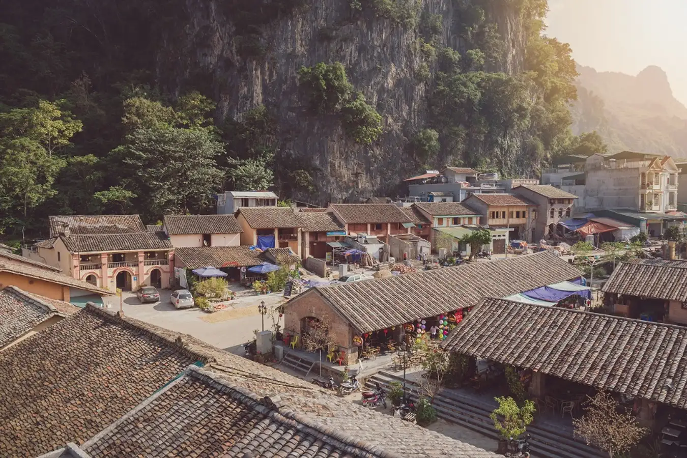 High-angle view of the ancient clay houses and tiled roofs of Dong Van Old Quarter nestled against a limestone mountain in Ha Giang, Vietnam.
