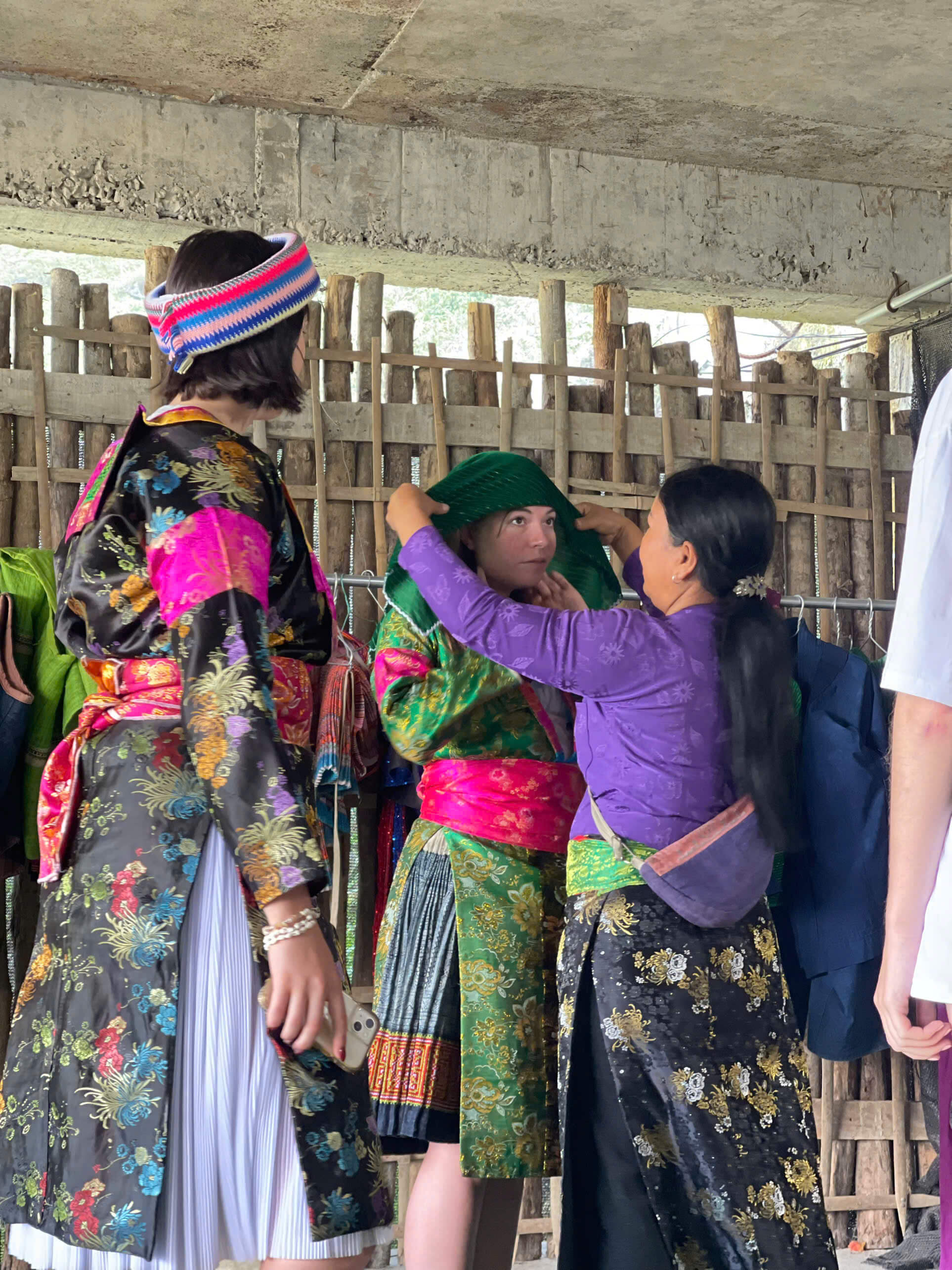 Travelers experiencing local culture by trying on intricate, hand-woven traditional ethnic costumes with the help of a local woman.
