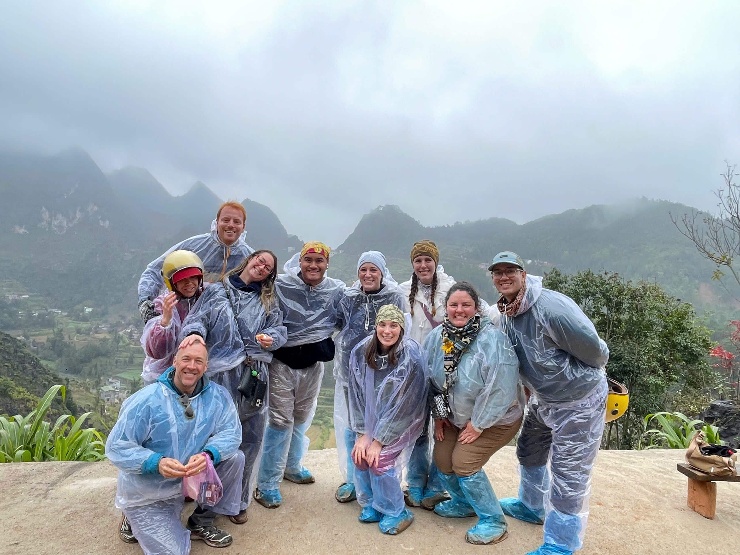 A small, diverse group of international travelers and local Easy Riders posing together at a scenic lookout in Ha Giang.