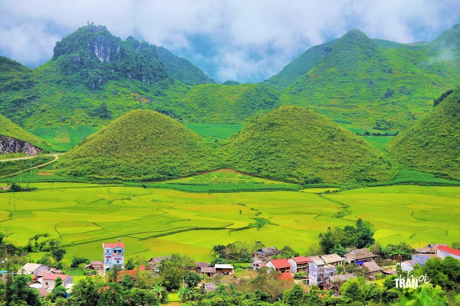 Panoramic view of the Quan Ba Twin Mountains, also known as Fairy Breast Mountains, surrounded by lush green rice fields and a small village in Ha Giang, Vietnam.