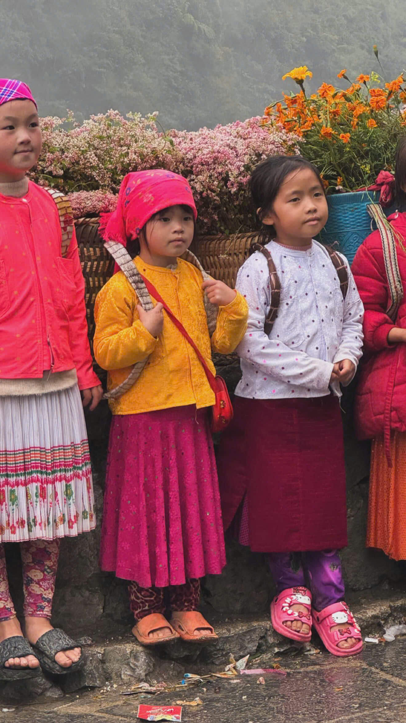 Local ethnic children in traditional clothing carrying baskets of flowers, used to illustrate responsible tourism practices in Ha Giang.