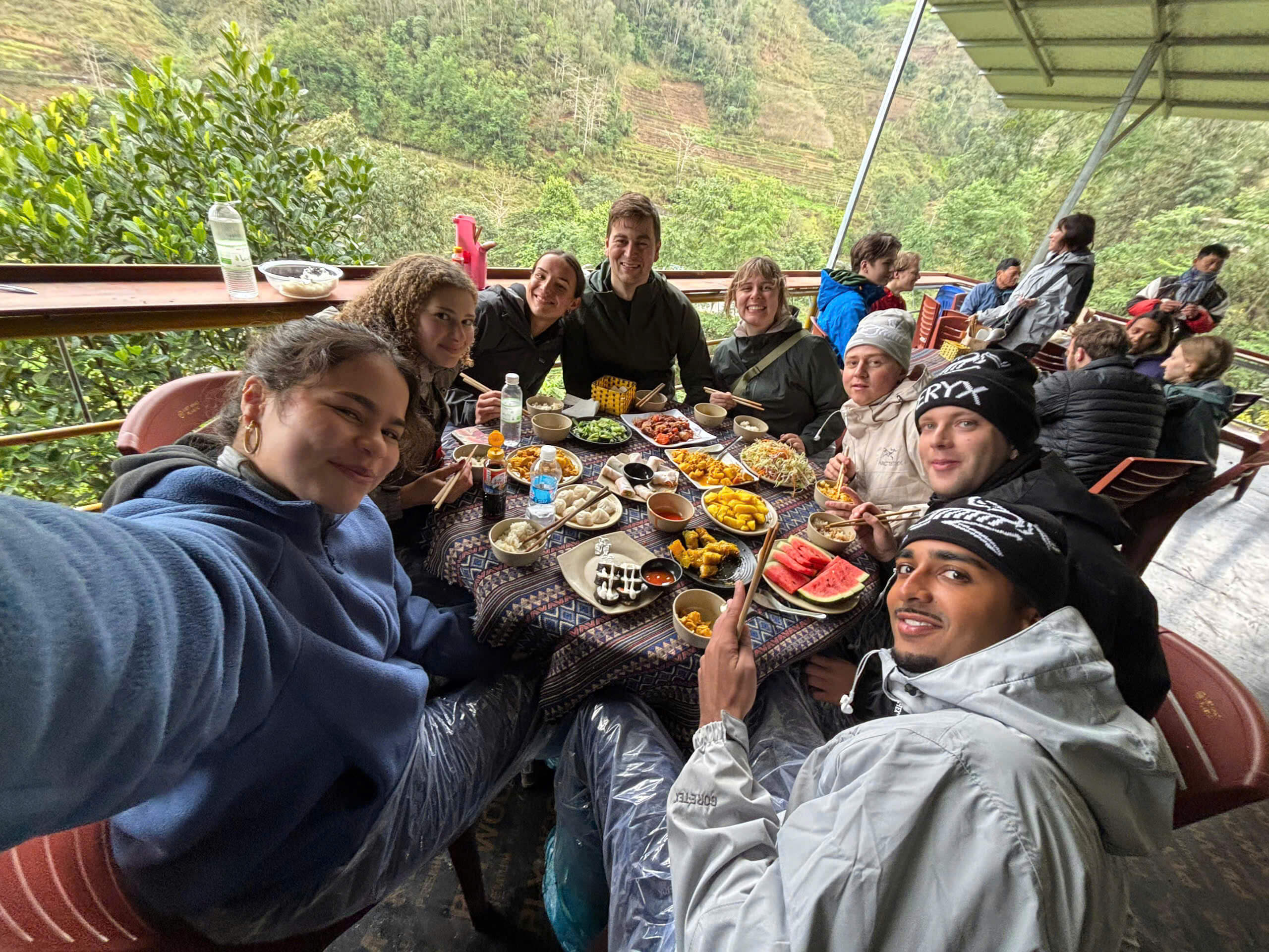 Group of tourists enjoying an authentic local meal with a scenic mountain view on a Ha Giang Loop tour