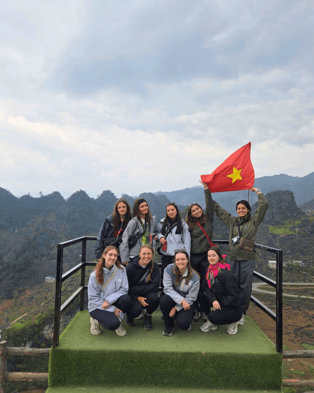Group of female backpackers waving the Vietnam flag from a scenic viewing platform on the Ha Giang Loop